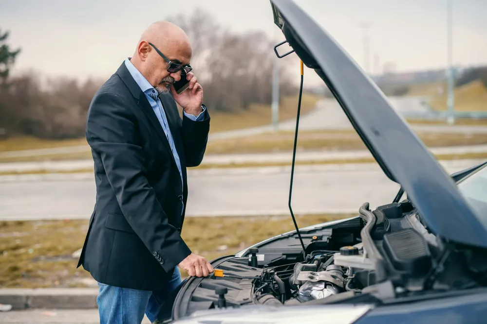 A driver on the phone beside a car with the bonnet raised